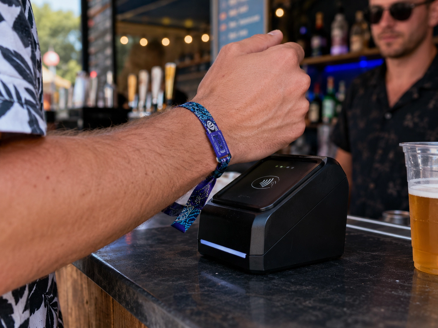 Close up of a guest tapping an RFID wristband on a cashless payment terminal at a festival bar
